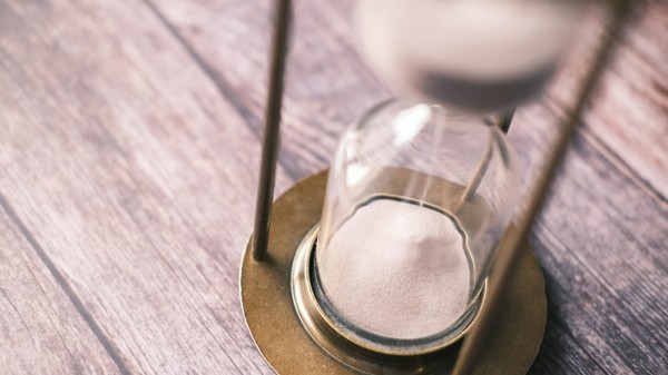 A close-up of sand passing through an hourglass on a wooden surface, representing a fixed coverage period.