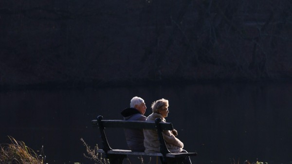 An older couple sitting together on a park bench in the sunshine, illustrating final-expense planning