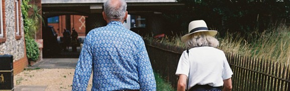 An older couple walking together on a paved path, illustrating a transition from job-based coverage