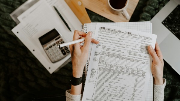 A person reviewing a U.S. tax form beside a calculator, notebook, and financial paperwork.