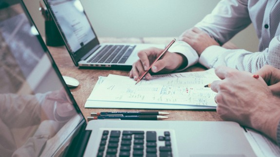 Two people reviewing handwritten notes beside laptops during a financial planning discussion.
