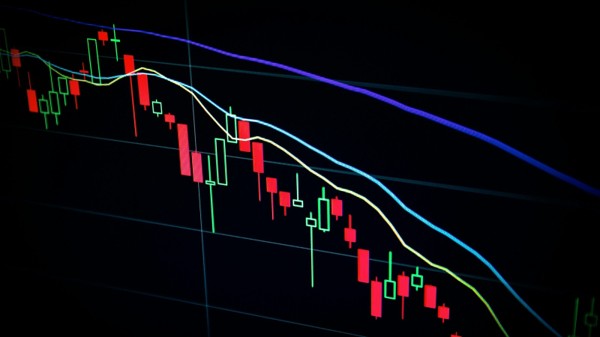 Red and green candlestick price movements on a dark market screen, illustrating market-linked policy variability.