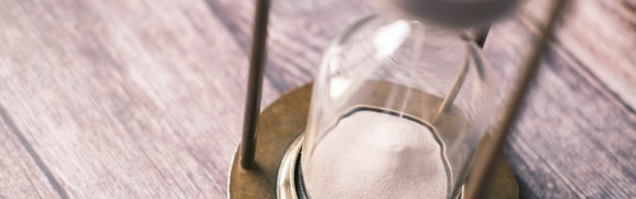 A close-up of sand passing through an hourglass on a wooden surface, illustrating the trade-offs involved in choosing a plan structure.