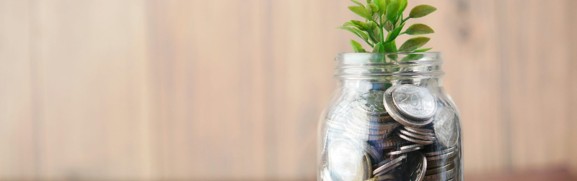 A small green plant in a glass jar of coins, illustrating employer spending and investment in employee health coverage.